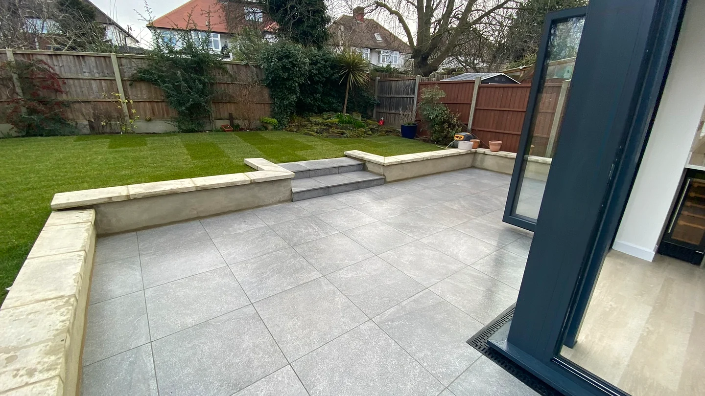 Porcelain garden patio with raised brick retaining wall and manicured lawn in Winchmore Hill N21